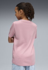 T-shirt en coton rose à manches courtes et col rond, avec une coupe décontractée et une texture lisse, associé à un jean bleu.