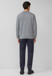 Szary sweter w paski z długim rękawem w połączeniu z ciemnoniebieskimi spodniami i czarnymi butami, prezentujący luźny krój i teksturowany wzór tkaniny.