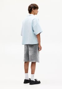 Camicia oversized azzurro chiaro, pantaloni corti grigi a fantasia, calze bianche e scarpe nere. I pantaloni corti presentano dettagliati disegni grafici su tutta la superficie.
