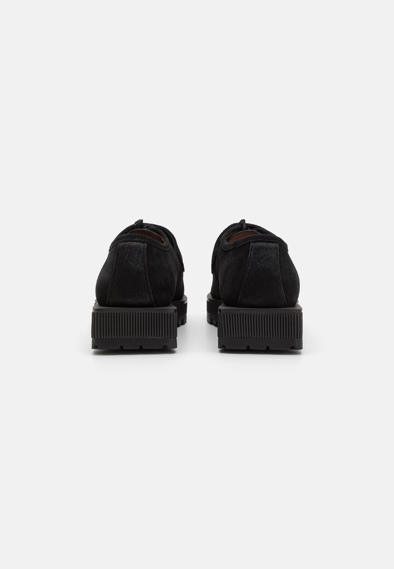 Chaussures en suede noir avec un panneau arrière texturé et une semelle en caoutchouc, dotées d'un design massif et strié pour une meilleure traction.