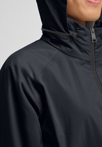 Leichter schwarzer Windbreaker mit Kapuze, ausgestattet mit einem Reißverschluss vorne und strukturiertem Stoff, geeignet für Outdoor-Aktivitäten.