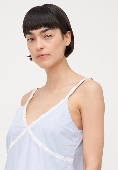 Light blue sleeveless top with a scalloped white lace trim, featuring a V-neck and a wrap design. Smooth texture, no visible patterns or hardware.