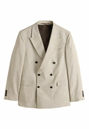 Mann trägt ein beigefarbenes Nadelstreifen-Sakko mit dunkelbraunem Einstecktuch über einem dunkelgrünen, zugeknöpften Hemd, vom Schulterbereich bis zu den Lippen beschnitten.