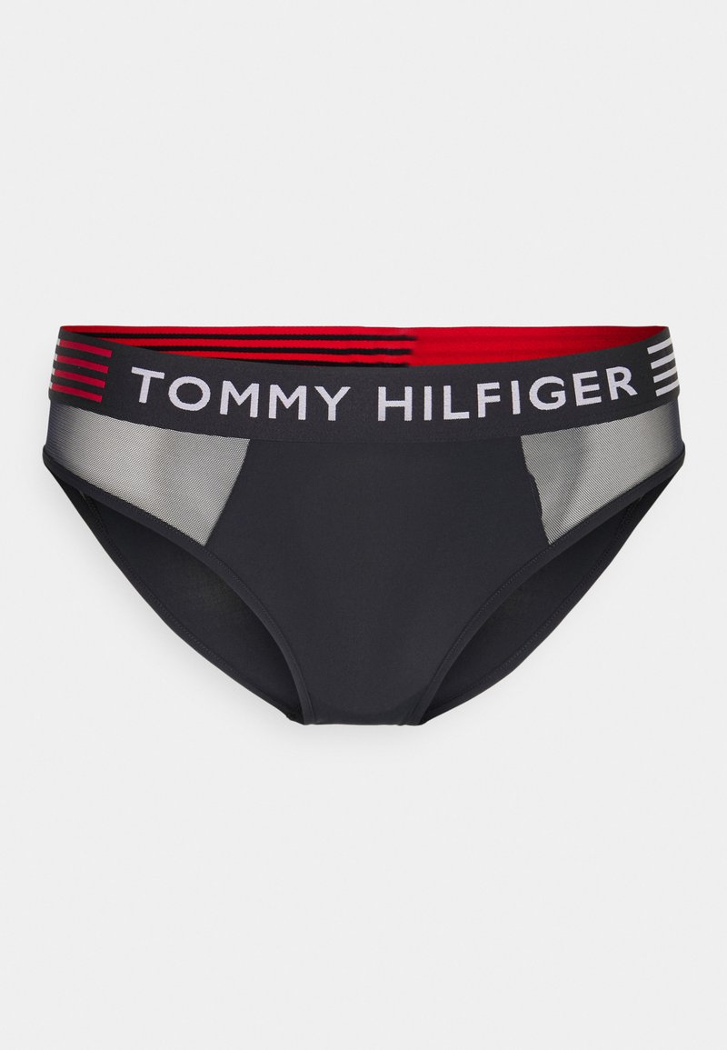 Bas de bikini noir avec une ceinture rayée rouge et blanche arborant le logo "TOMMY HILFIGER". Le matériau semble lisse avec une touche de maille.