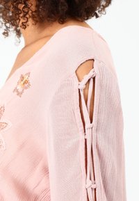 Top rosa intrecciato con ricami floreali, caratterizzato da un dettaglio con spalla scoperta fissato da un laccio e un tessuto textured.