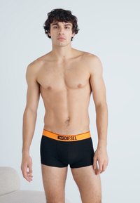 Boxers noirs avec une ceinture orange portant l'inscription "DIESEL." Le matériau semble lisse et extensible, s'ajustant parfaitement. Design simple.