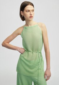 Top senza maniche verde chiaro con una finitura testurizzata, dotato di spalline sottili e un dettaglio con laccetto in vita per regolazione e vestibilità.