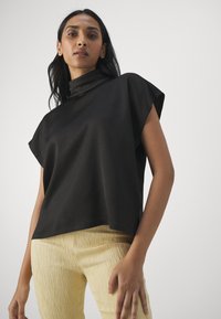 Top corto nero a maniche corte con colletto alto, realizzato in tessuto liscio. Abbinato a pantaloni giallo chiaro con texture. Design semplice e moderno.