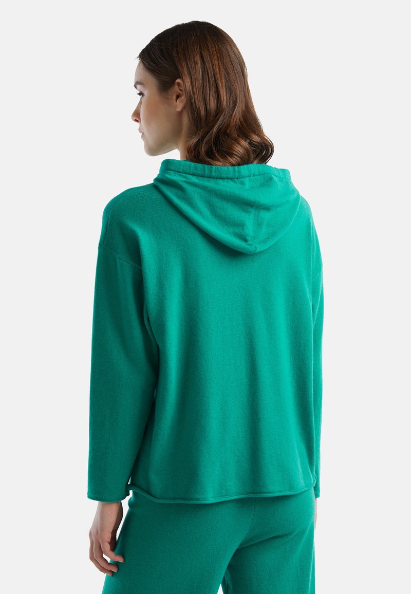 Sudadera de forro polar verde con un corte relajado, que cuenta con capucha, mangas largas y una textura suave, combinada con pantalones verdes a juego.