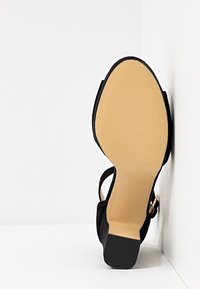 Sandale noire pour femme avec une semelle beige et un petit talon bloc, vue de dessous sur fond blanc.
