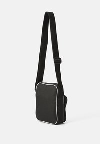Bolso bandolera negro hecho de tejido duradero, con ribetes blancos, de forma plana y una correa ajustable con hebilla.
