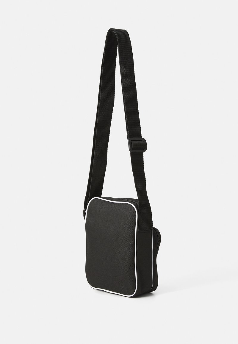 Czarna torba crossbody wykonana z trwałego materiału, z białymi akcentami, płaskim kształtem oraz regulowanym paskiem z klamrą.