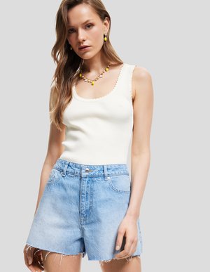 Vit ribbad t-shirt med scallop-kant, ihop med högmidjade ljusblå denimshorts med fransade sömmar. Accessoarer inkluderar gult smycke.
