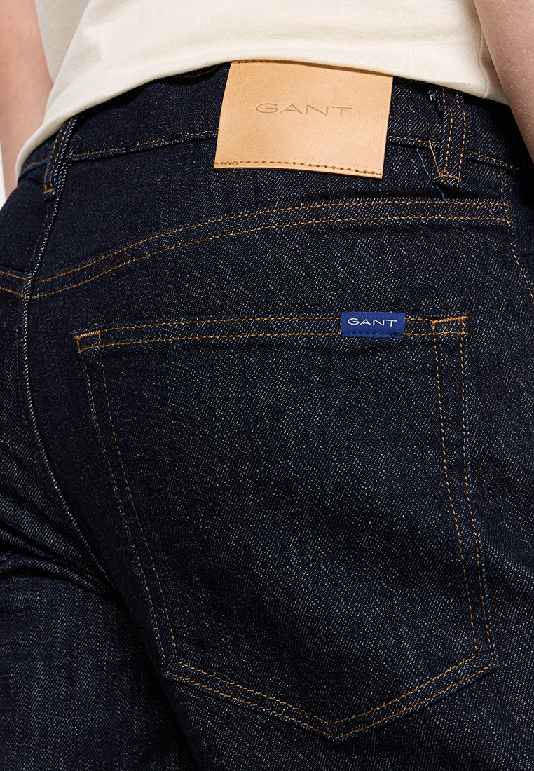 Dunkelblaue Jeans aus Denim mit orangefarbenen Nähten, einem Leder-Patch der Marke GANT am Taillenbund und einem kleinen blauen GANT-Stofflabel auf der Gesäßtasche.