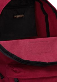 Interno dello zaino in tela rossa con una tasca con zip nera e una fodera liscia. Gli accessori includono un'etichetta del marchio e una toppa di tessuto.
