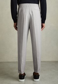Homme portant un pantalon sur mesure gris clair avec une taille élastique, un haut noir à manches longues et des baskets noires à semelles blanches, vu de dos.