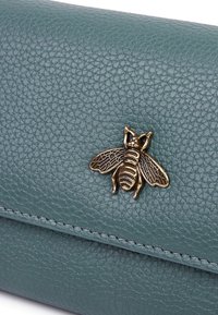 Portafoglio in pelle teal con una finitura testurizzata, adornato da un dettagliato emblema di ape dorata sul fronte per un tocco di interesse visivo.