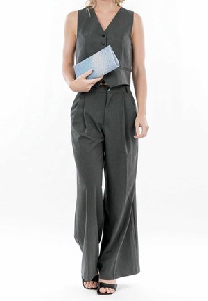 Gilet gris sur mesure et pantalon large en tissu léger. Le modèle tient une pochette bleu clair avec un dégradé scintillant.