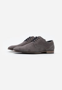 Gray suede lace-up shoes with a smooth texture, pointed toe, and contrasting brown sole. Features stitched detailing on the upper.