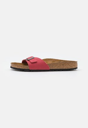 Rød ruskinds Birkenstock-sandal med justerbar rem, korksål og sort tekstureret sål på en ensfarvet hvid baggrund.