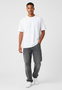 T-shirt bianco a maniche corte abbinato a jeans dritti grigi e sneaker bianche. Il tessuto sembra liscio con una vestibilità comoda e senza motivi visibili.
