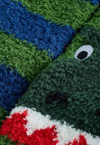 Tessuto in peluche testurizzato nei colori verde, blu e bianco, con un design di dinosauro con occhi e denti ricamati. Finitura morbida e soffice.