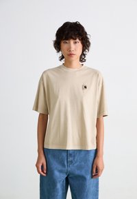 T-shirt en coton beige avec une coupe décontractée, des manches courtes et un col rond. Présente un petit logo brodé sur la poitrine gauche.