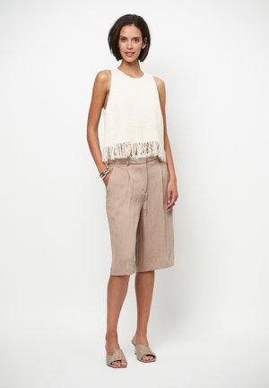 Crèmewitte gebreide tanktop met franjerand, gecombineerd met beige shorts met hoge taille. Model draagt lichtbruine slide-on schoenen. Eenvoudige, ontspannen pasvorm.