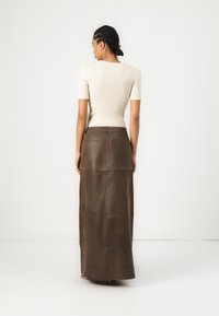 Hnědá kožená maxi sukně s vysokým pasem a zadními kapsami, v kombinaci s přiléhavým krémovým tričkem s krátkými rukávy, vytvářející elegantní siluetu.