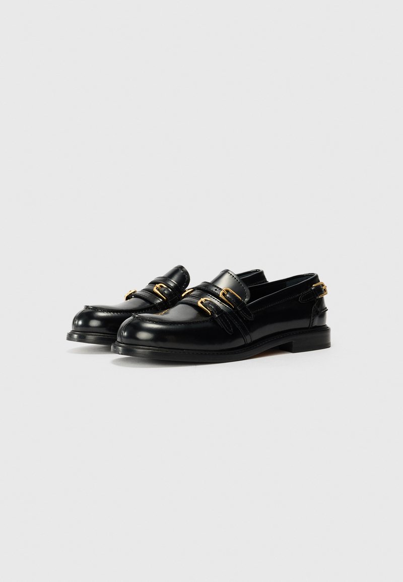 Zwarte leren loafers met dubbele bandontwerp en goudkleurige hardware, ronde neus en lage gestapelde hak. Glad materiaal overal.