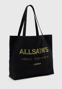 Juodas drobės pirkinių krepšys su dviem rankenomis, su ryškiais užrašais "ALLSAINTS" ir "LONDON" metaliniais akcentais. Užrašai keliomis kalbomis.