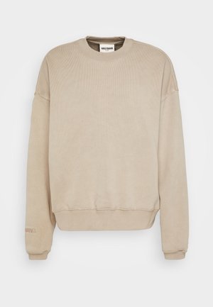 Sweat-shirt beige à manches longues avec col rond, poignets et bas côtelés, texture subtile et petit logo brodé près du poignet gauche.