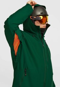 Groene waterdichte jas met een ritssluiting aan de voorkant en een oranje mesh voering. Heeft een capuchon, zijzakken en versterkte naden. Geschikt voor buitenactiviteiten.