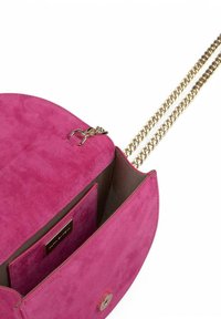 Bolso cruzado de ante rosa con una correa de cadena dorada, cierre magnético y un bolsillo interior. Textura suave y diseño redondeado.