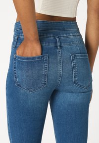 Jeans de mezclilla elástica en azul oscuro, con una cintura alta, dos bolsillos traseros y una textura suave con sutiles detalles desgastados.