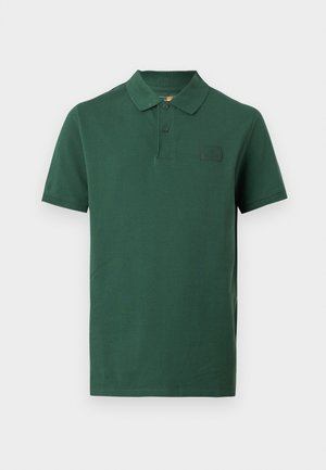 Tricou polo cu mâneci scurte, de culoare verde închis, cu două nasturi și o mică etichetă cu logo-ul Timberland pe pieptul stâng.