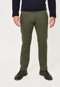 Olivgrüne Chinos aus weichem Stoff mit geradem Bein und Taschen vorne. Kombiniert mit schwarzen Schnürschuhen.