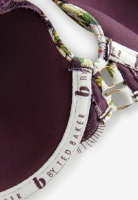 Podprsenka v tmavej burgundskej farbe s kvetinovým ozdobením, vycpanými košíčkami a zlatými komponentmi, s hladkým materiálom a textúrovanou čipkovanou stranou.