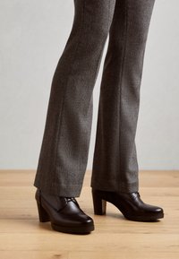 Pruunist nahast kontsakingad, millel on ümar varvas, tekstuuriga pealispind ja tagasihoidlik platvorm, kombineeritud herringbone-mustriga pükstega.