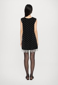 Μαύρο βελούδινο φόρεμα με λευκή στιλιζαρισμένη σχεδίαση, κοντό στρίφωμα με φούντες, και αμάνικο σχέδιο, συνδυασμένο με διάφανα μαύρα καλσόν.