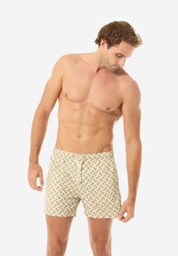 Pantaloni da bagno beige con un motivo astratto bianco, vita con coulisse e tessuto testurizzato, che mostrano una vestibilità rilassata e una lunghezza fino al ginocchio.