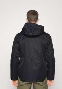 Giacca nera impermeabile con cappuccio, caratterizzata da una texture liscia e un retro leggermente più lungo, progettata con accenti minimalisti.