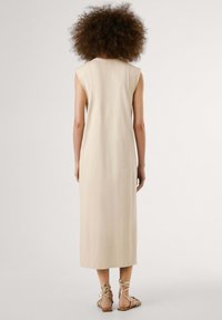Beige ärmlös maxiklänning gjord av mjukt material, med en avslappnad passform, rak skärning och en minimalistisk design.
