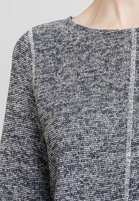 Sweter z teksturowanym wzorem dzianiny w ciemnoniebieskim i białym kolorze, z okrągłym dekoltem i kontrastowym jasnym szwem wzdłuż szwów.