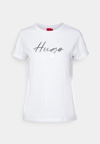 Vit bomulls-t-shirt med korta ärmar och rund halsringning. Har en silverfärgad "Hugo"-logotyp tryckt över bröstet.
