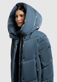 Gewatteerde jas van glanzend blauw materiaal, met een grote, gestructureerde capuchon, een rits aan de voorkant en zijzakken met elegante zwarte accenten.