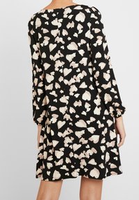 Svart klänning med ett hjärtformat blommönster i beige och krämfärg. Långa puffärmar och rak skärning med en sömdetalj på baksidan.