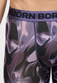 Κοντινό πλάνο μοβ και μαύρων boxer briefs με φαρδιά ζώνη που φέρει το όνομα της μάρκας Björn Borg με μαύρα γράμματα.