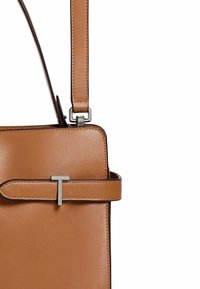 Borsa a tracolla in pelle marrone con forma rettangolare, lunga tracolla regolabile e un accento in metallo argentato che presenta la lettera "T".