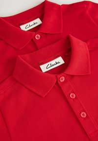 Camisas polo rojas con cuellos planos, tres botones y una tela texturizada. Las etiquetas muestran la marca "Clarks" en el collar.